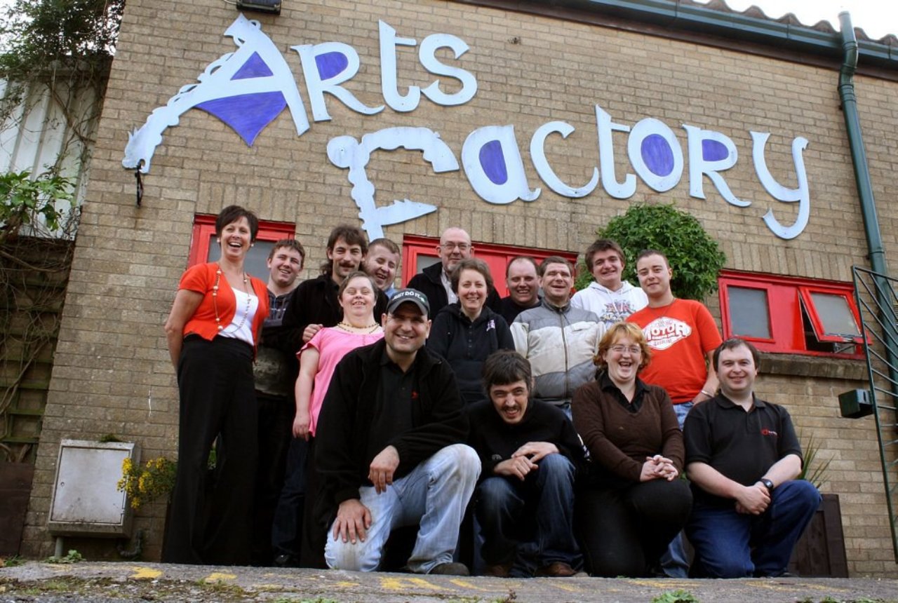 A group of people standing in front of a building with the words 'Arts Factory' behind them