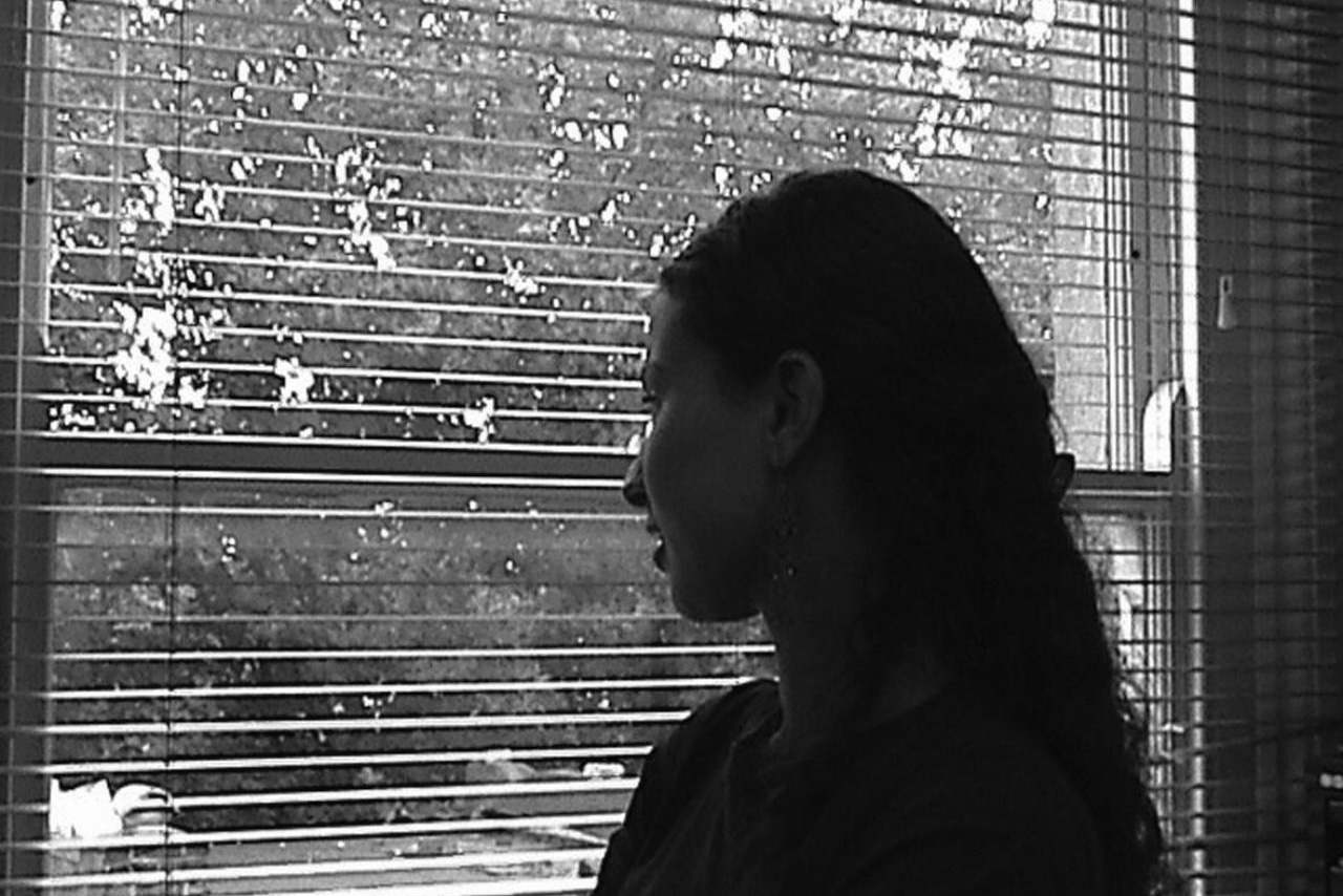 A woman looking our of an office blind, in black and white